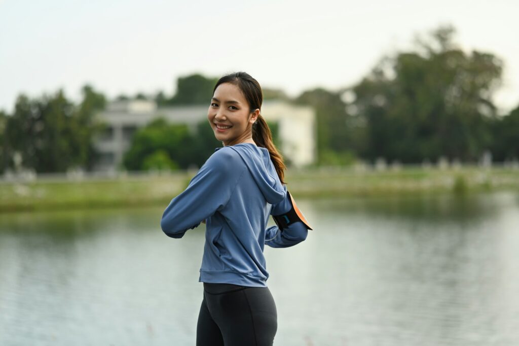 Active sporty female warming up body before workout session at the park in early morning.