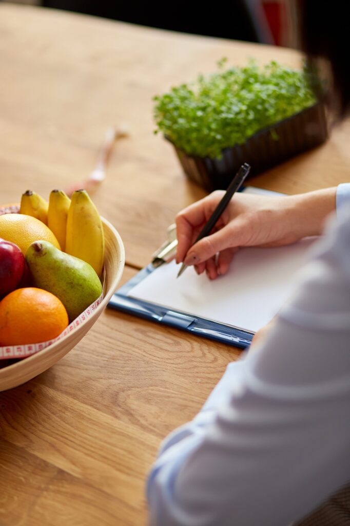 Nutritionist, dietitian woman writing a diet plan, with healthy vegetables and fruits